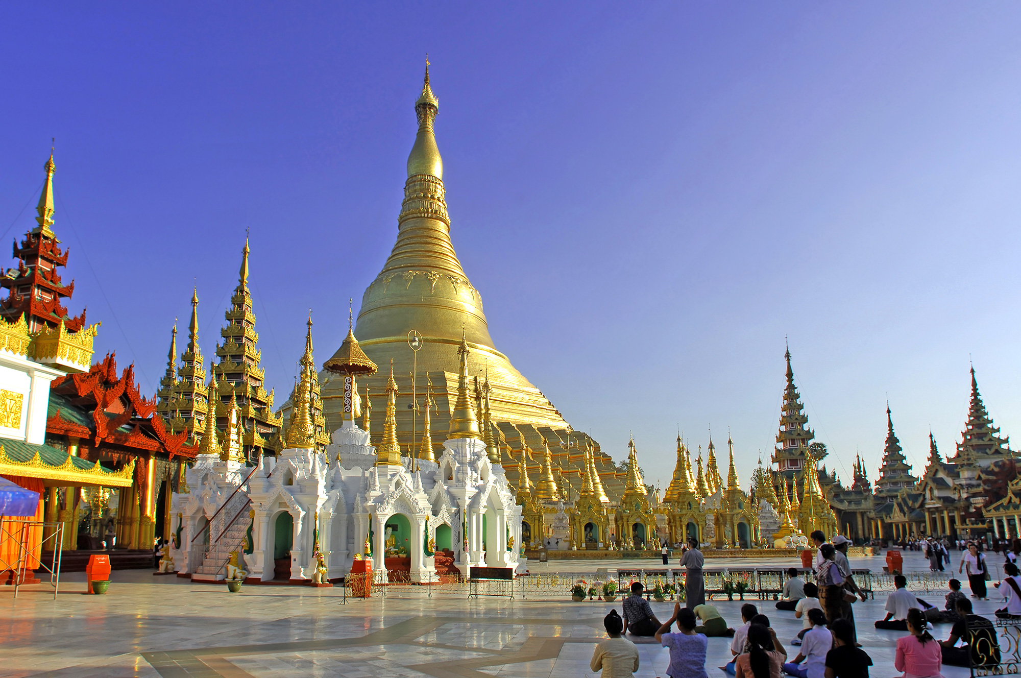 a group of people standing in front of a large gold and white building with Shwedagon Pagoda in the background