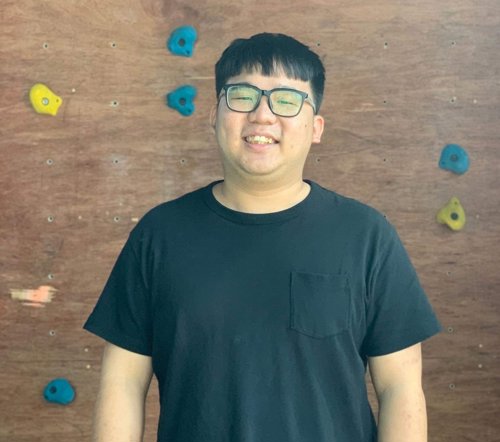 a man in glasses smiling in front of a rock climbing wall