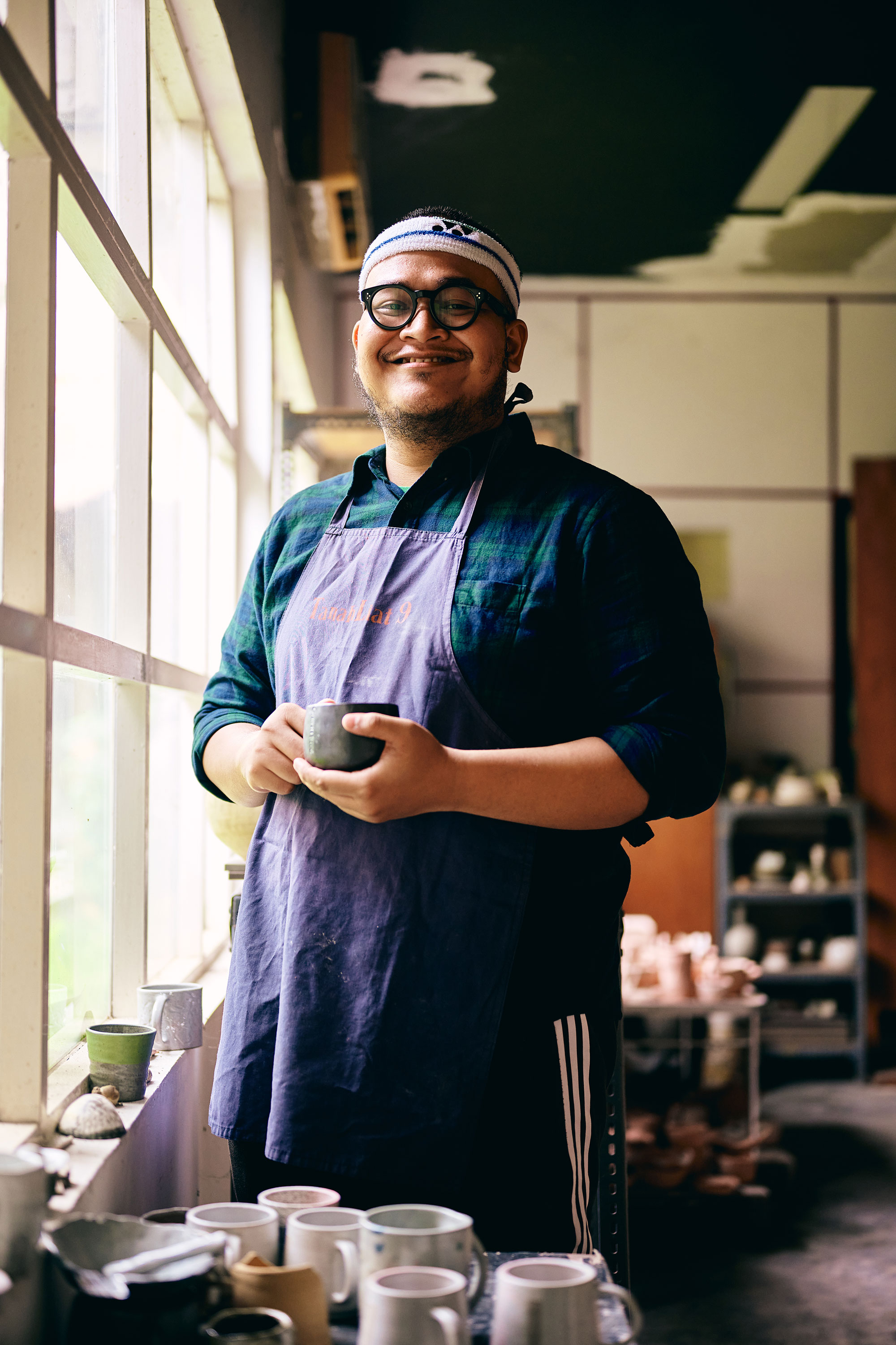 a man wearing glasses and a apron holding a cup