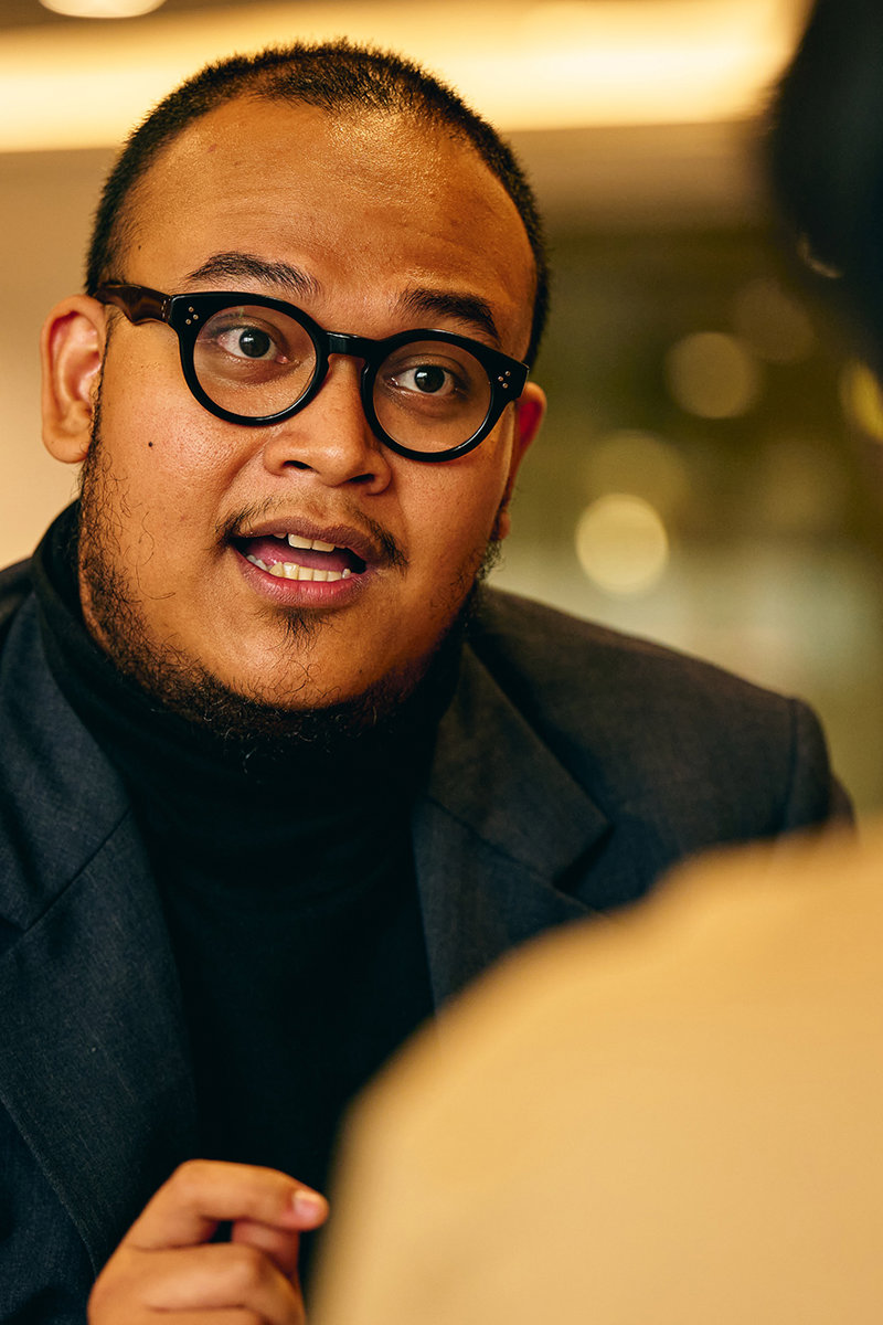 a man in a suit and glasses talking to another man