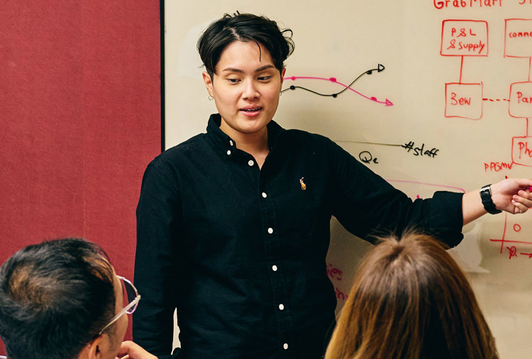 a woman pointing at a whiteboard with people in the background