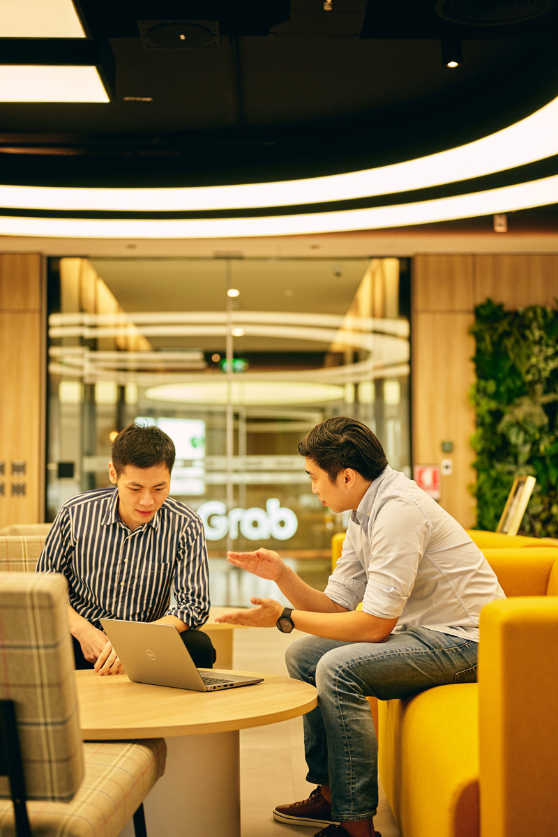 two men sitting on a couch looking at a laptop